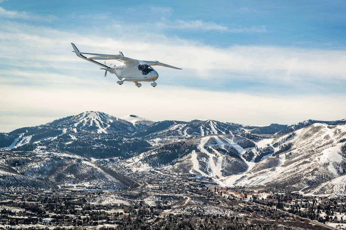 BETA Technologies' electric aircraft ALIA flying over a snowy range of mountains.