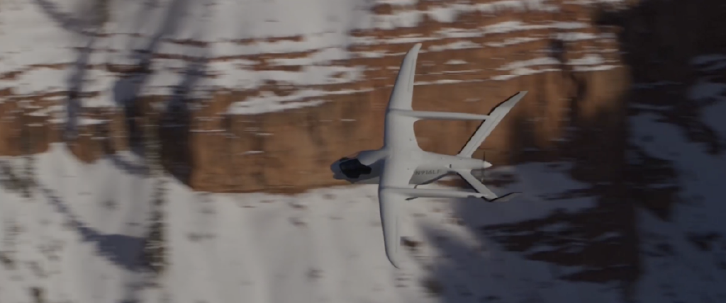 An experimental electric aircraft, made by Beta Technologies, flying with the Utah red rocks, covered in snow, in the background.